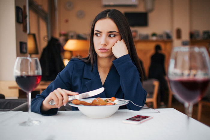Woman looking upset at restaurant, reflecting tension related to man undermining wife’s job and defensiveness. Woman looking upset at restaurant, reflecting tension related to man undermining wife’s job and defensiveness.
