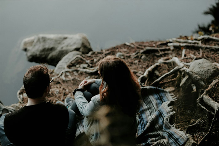 Couple sitting silently by a lake, depicting tension after a woman's husband leaves her unexpectedly. Couple sitting silently by a lake, depicting tension after a woman's husband leaves her unexpectedly.