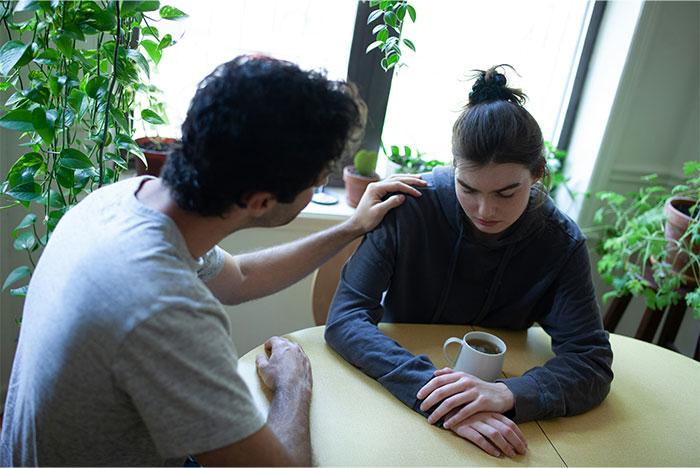 Husband comforting wife at a table, woman looking down sadly after being hit on for the first time.