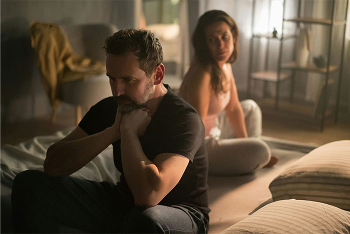 Man and woman sitting apart on bed looking upset, illustrating woman's husband leaves her after being hit on. Man and woman sitting apart on bed looking upset, illustrating woman's husband leaves her after being hit on.