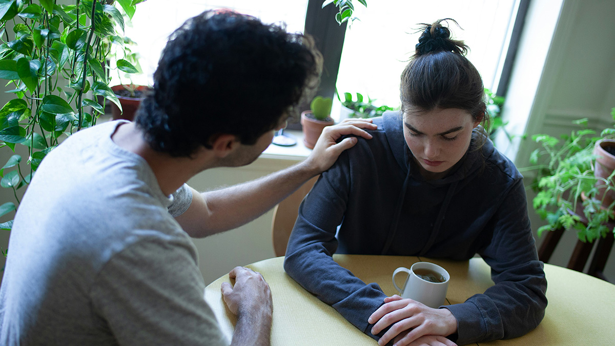 Husband comforting upset wife at a kitchen table with a cup of tea, reflecting tension after being hit on for the first time.