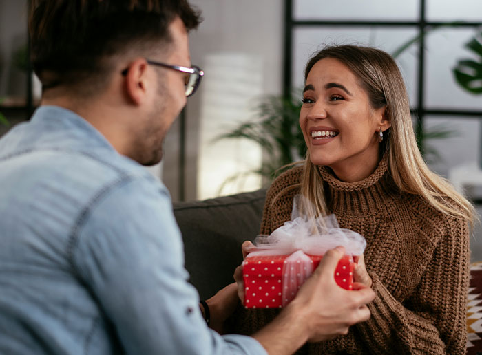 Woman surprises husband with pregnancy test as birthday gift, both sharing an emotional moment on a cozy couch indoors. Woman surprises husband with pregnancy test as birthday gift, both sharing an emotional moment on a cozy couch indoors.