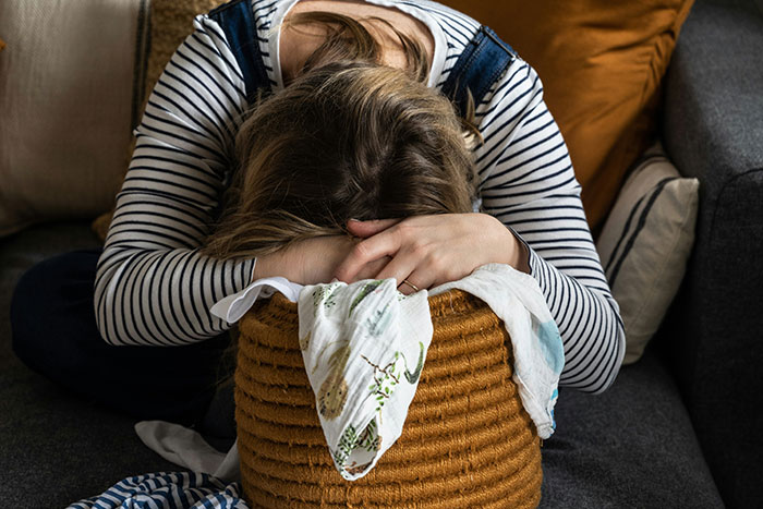 Woman overwhelmed and resting her head on a basket, illustrating struggle with husband refusing to help with child care responsibilities. Woman overwhelmed and resting her head on a basket, illustrating struggle with husband refusing to help with child care responsibilities.