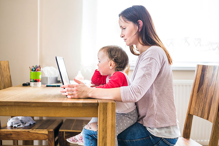 Mother and child sitting at a wooden table using a tablet, illustrating child care and parenting challenges. Mother and child sitting at a wooden table using a tablet, illustrating child care and parenting challenges.