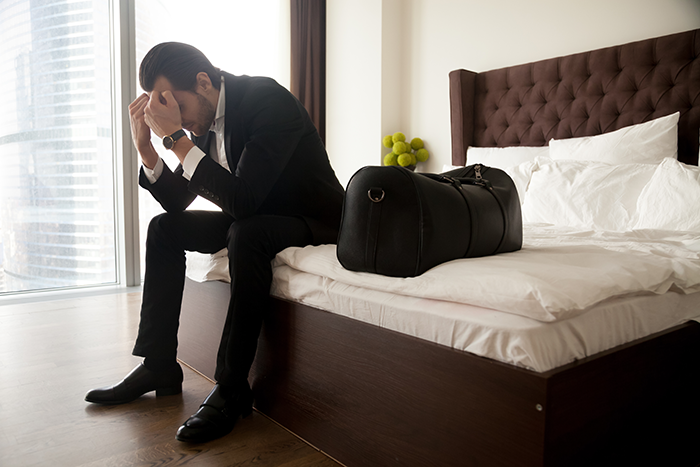 Man in suit sitting on bed with travel bag, looking distressed after wife's cancer diagnosis impacts plans for biological kids. Man in suit sitting on bed with travel bag, looking distressed after wife's cancer diagnosis impacts plans for biological kids.