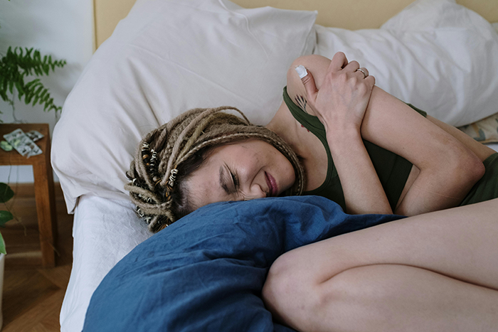Woman with dreadlocks lying in bed, clutching herself in pain, representing emotional distress after cancer diagnosis. Woman with dreadlocks lying in bed, clutching herself in pain, representing emotional distress after cancer diagnosis.