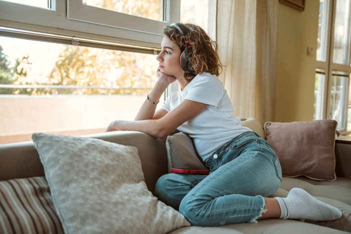 Woman with headphones sitting on couch, looking thoughtful and reflective about ending gaming days for fiancé. Woman with headphones sitting on couch, looking thoughtful and reflective about ending gaming days for fiancé.