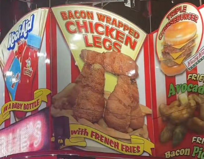 Fair food stand featuring bacon wrapped chicken legs with french fries and a triple cheeseburger at a county fair. Fair food stand featuring bacon wrapped chicken legs with french fries and a triple cheeseburger at a county fair.