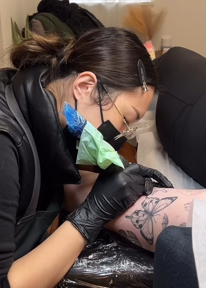 Tattoo artist wearing gloves and mask creating a detailed butterfly tattoo on a client's arm during the tattoo boom. Tattoo artist wearing gloves and mask creating a detailed butterfly tattoo on a client's arm during the tattoo boom.