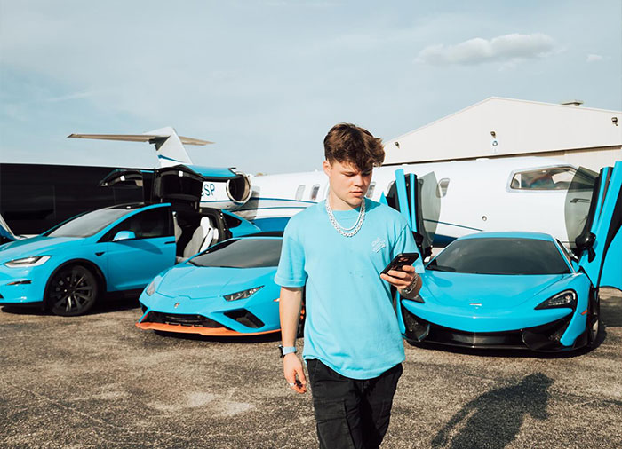 Jack Doherty in a blue shirt beside luxury cars and a private jet, symbolizing Jack Doherty net worth growth and success.