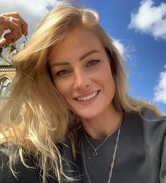 Smiling experienced skydiver with blonde hair outdoors under blue sky, wearing layered necklaces and dark sweatshirt. Smiling experienced skydiver with blonde hair outdoors under blue sky, wearing layered necklaces and dark sweatshirt.