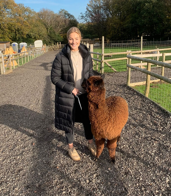 Woman with alpaca on a farm path, representing an experienced skydiver with over 400 flights in a casual outdoor setting. Woman with alpaca on a farm path, representing an experienced skydiver with over 400 flights in a casual outdoor setting.