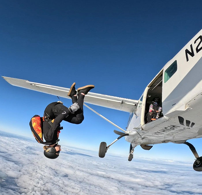 Experienced skydiver wearing helmet and gear, performing a flip while jumping from a small plane above the clouds. Experienced skydiver wearing helmet and gear, performing a flip while jumping from a small plane above the clouds.