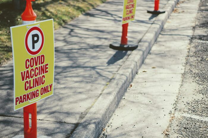 Parking area signs for a COVID vaccine clinic aligned along a sidewalk under sunlight and shadows.