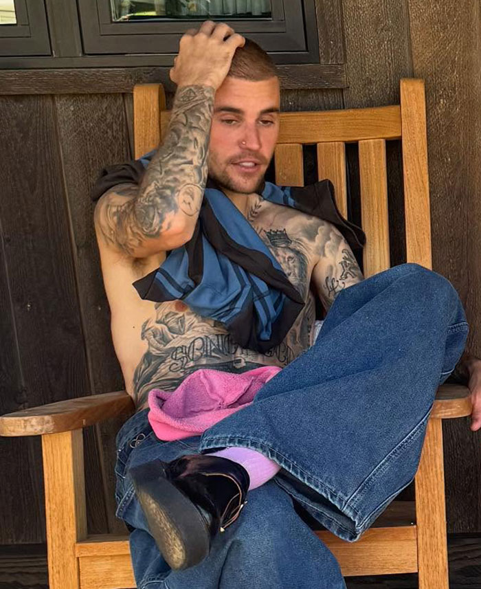 Justin Bieber sitting shirtless on a wooden chair showing tattoos and casual denim pants in a relaxed pose. Justin Bieber sitting shirtless on a wooden chair showing tattoos and casual denim pants in a relaxed pose.