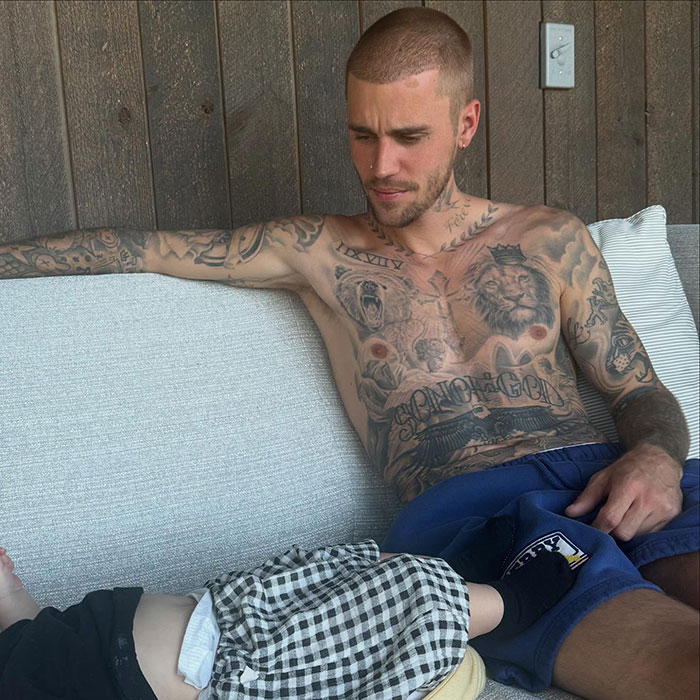 Justin Bieber shirtless with tattoos, sitting next to his son during a holiday, sparking parenting debate over smoking. Justin Bieber shirtless with tattoos, sitting next to his son during a holiday, sparking parenting debate over smoking.