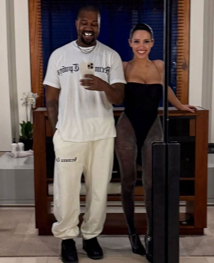 Kanye West's friend taking a mirror selfie with Bianca Censori wearing a revealing outfit in a modern indoor setting. Kanye West's friend taking a mirror selfie with Bianca Censori wearing a revealing outfit in a modern indoor setting.