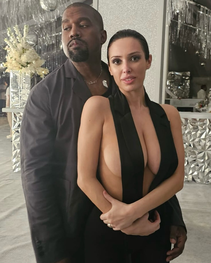 Kanye West and Bianca Censori posing together indoors with reflective and floral decor in the background. Kanye West and Bianca Censori posing together indoors with reflective and floral decor in the background.
