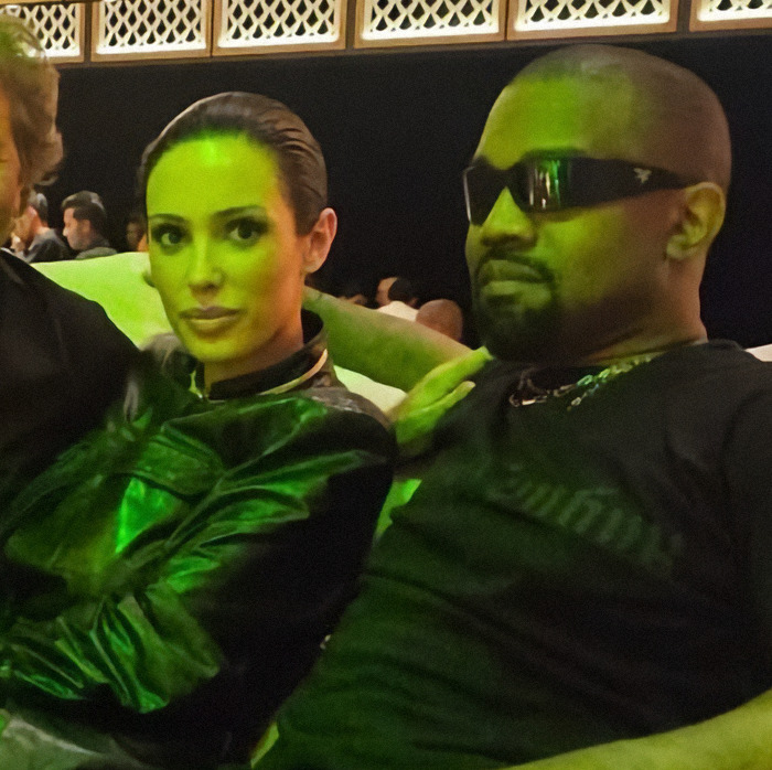 Kanye West and Bianca Censori sitting together in a dimly lit venue, highlighting Kanye West subservient post. Kanye West and Bianca Censori sitting together in a dimly lit venue, highlighting Kanye West subservient post.