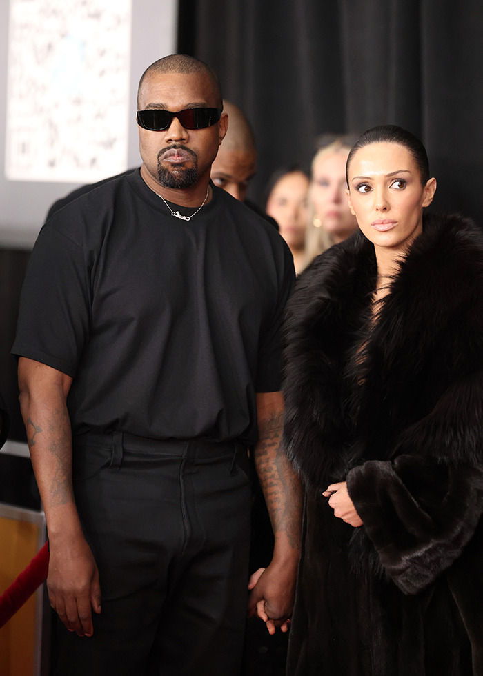 Kanye West wearing black and holding hands with Bianca Censori in a fur coat at an event. Kanye West wearing black and holding hands with Bianca Censori in a fur coat at an event.