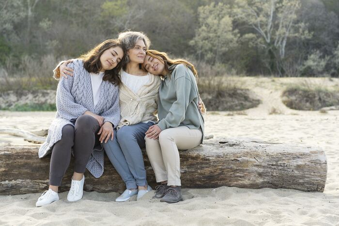 Three women sitting on a log outdoors, showing unhinged parents in a calm, supportive moment with nature background.