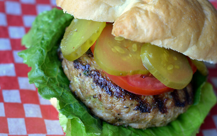 Grilled burger with lettuce, tomato, and pickles on a bun, showcasing a fresh and appetizing meal.