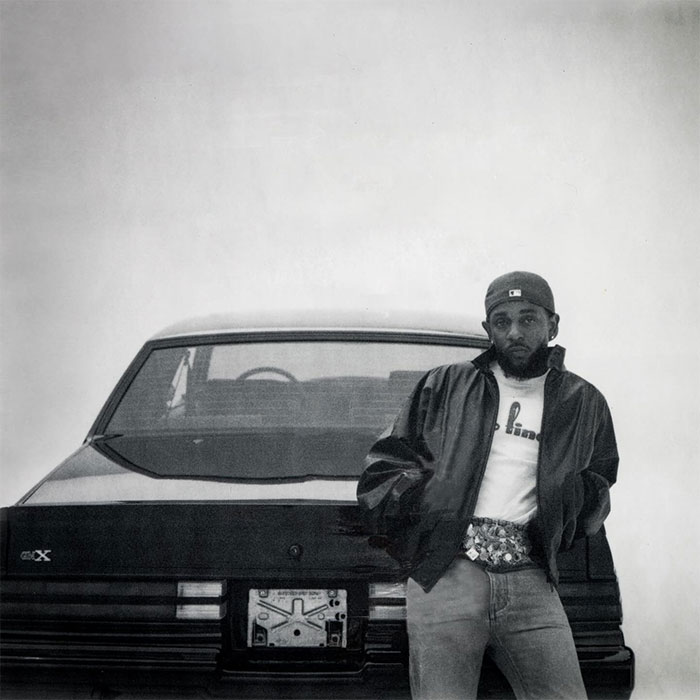 Kendrick Lamar leaning against a car, wearing a cap and jacket, symbolizing net worth and success in hip hop.