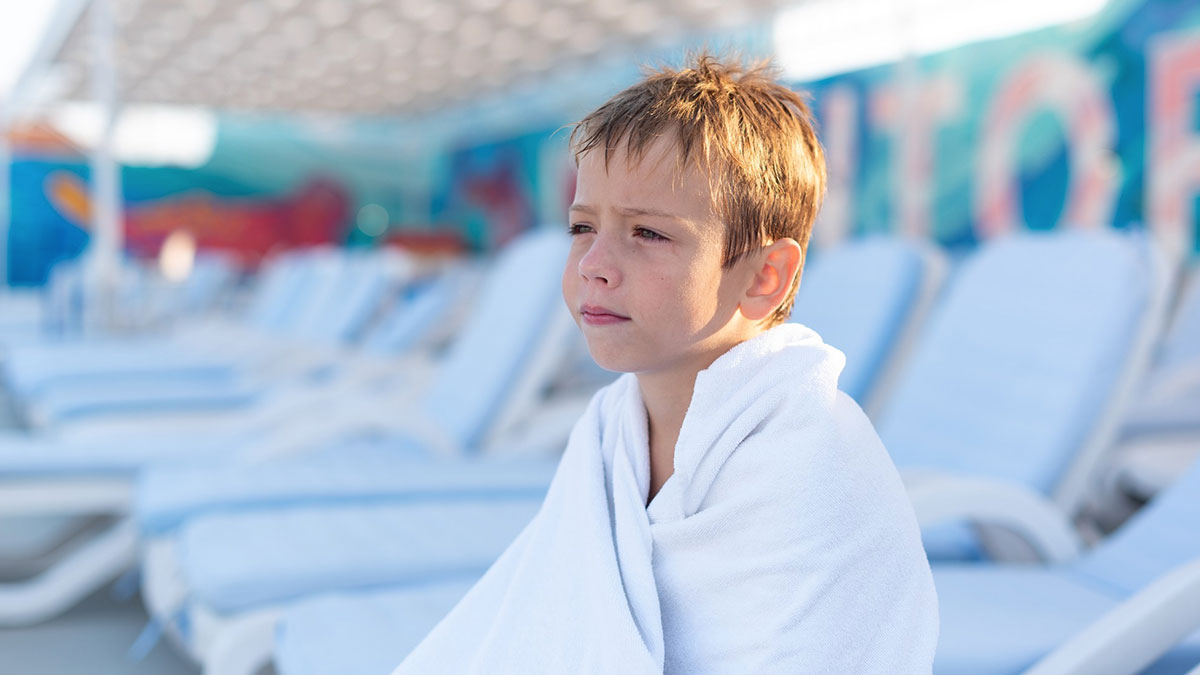 Young boy wrapped in towel sitting by empty condo pool area, looking sad after being told non-residents canu2019t use the pool