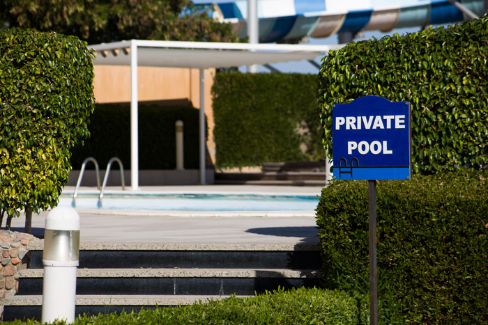 Condo pool with private pool sign, surrounded by greenery and steps leading to the water on a sunny day.