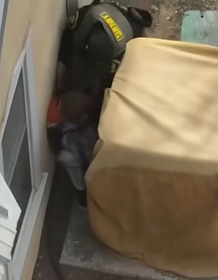 Police officer detaining a child in pajamas near a building, involving cops and children with alleged weapons refusal. Police officer detaining a child in pajamas near a building, involving cops and children with alleged weapons refusal.