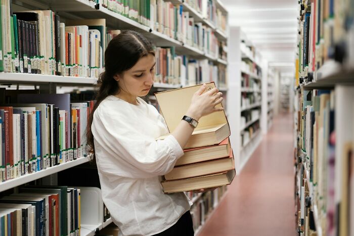 Young woman holding a stack of books in a library aisle, representing industry secrets and behind closed doors insights.