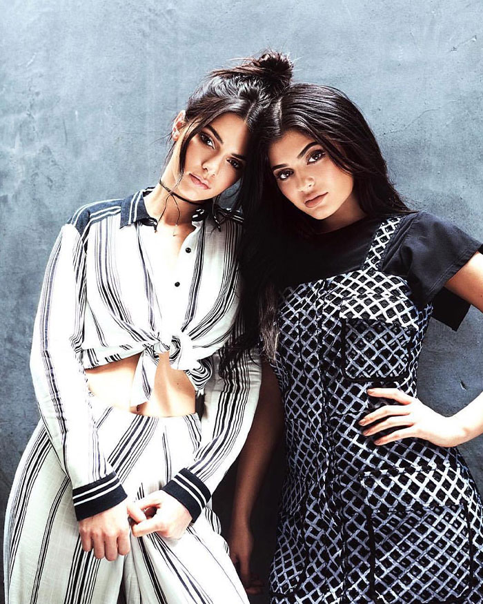 Two women posing stylishly against a textured wall, illustrating Kylie Jenner’s net worth and financial status update.