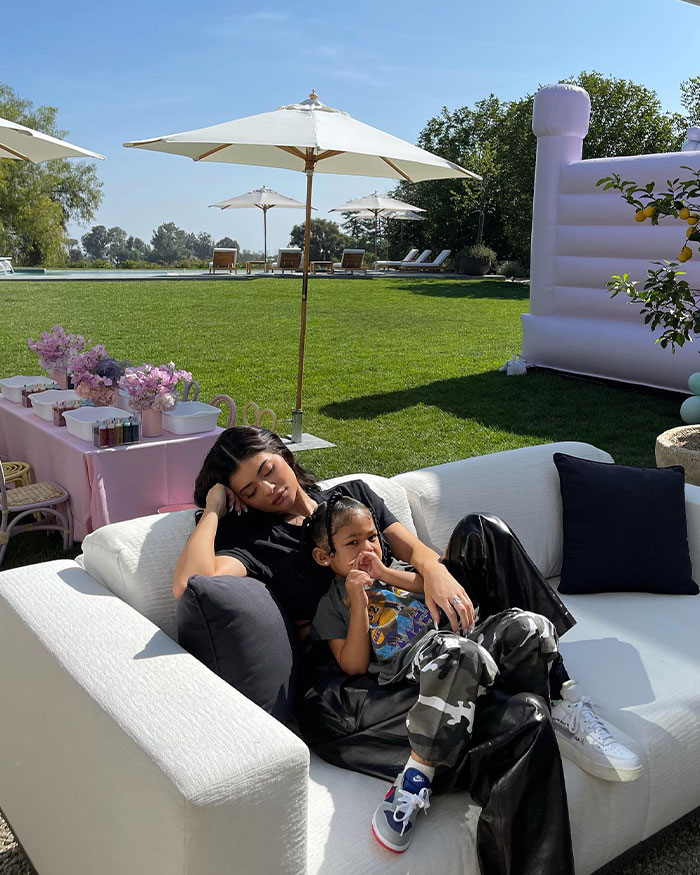 Kylie Jenner relaxing on a white couch outdoors with her child, highlighting Kylie Jenner net worth and lifestyle.