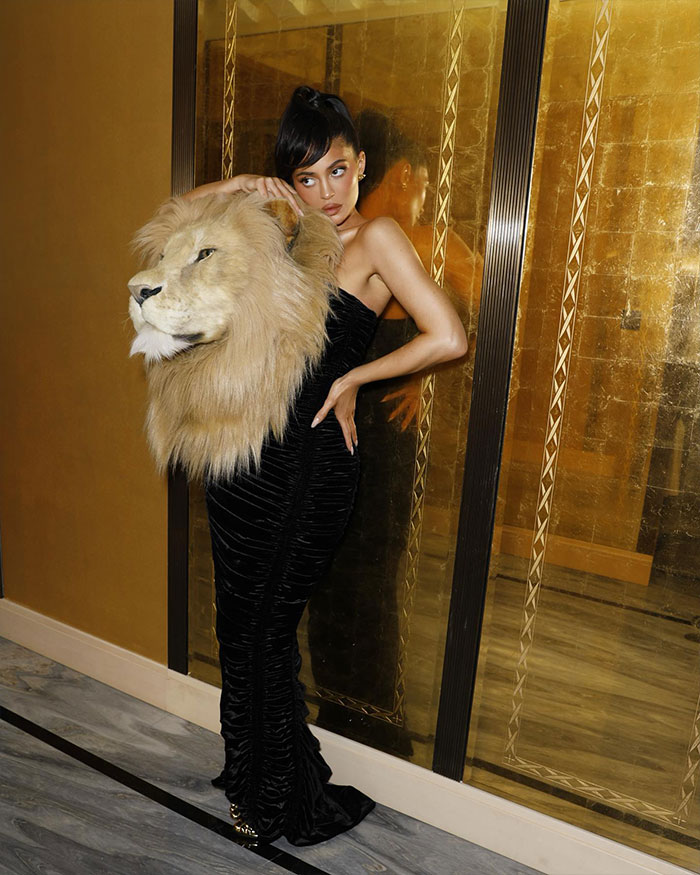 Kylie Jenner posing in a black dress holding a large lion head prop reflecting her net worth status update.