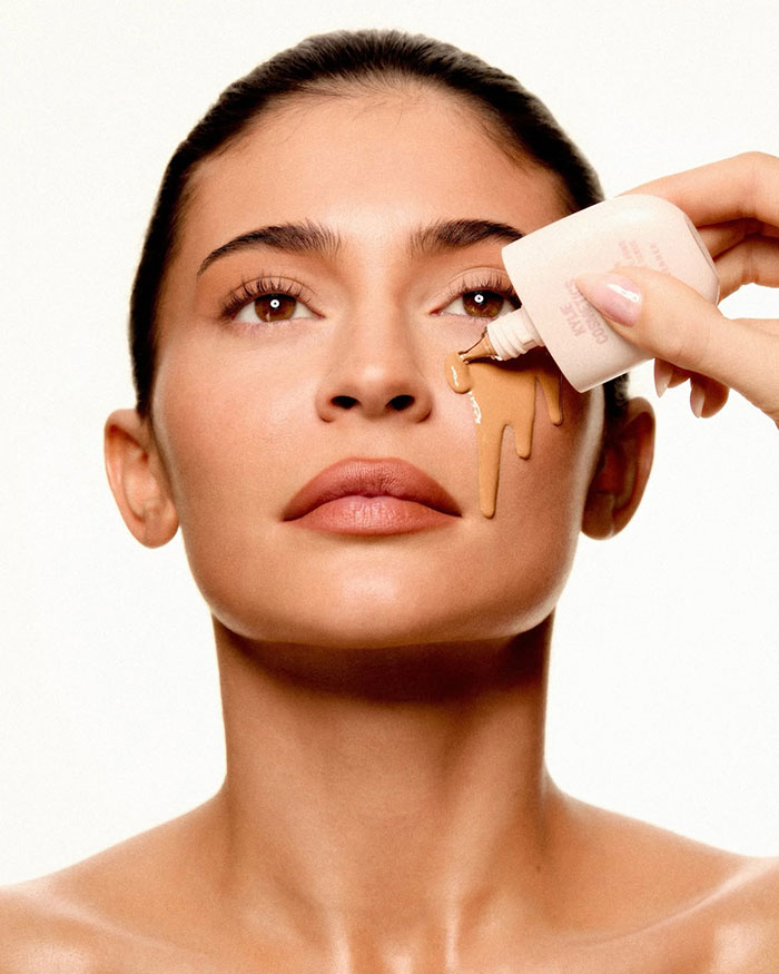 Kylie Jenner applying foundation makeup on her face, highlighting her beauty and net worth status.