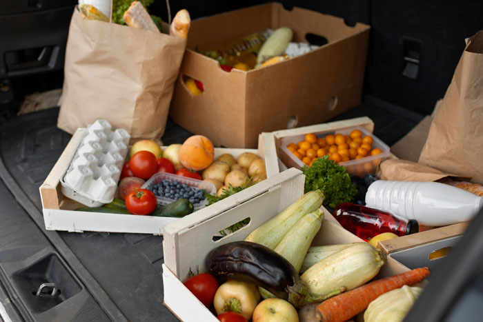 Various fresh grocery items including vegetables and fruits packed in crates and paper bags in a car trunk. Various fresh grocery items including vegetables and fruits packed in crates and paper bags in a car trunk.