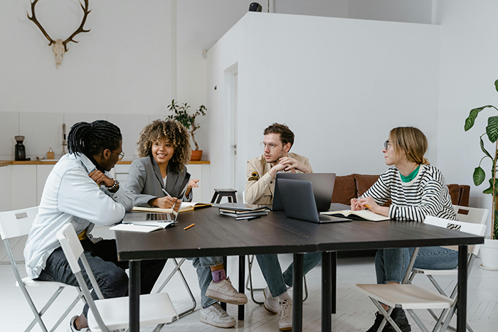 A group of employees discussing work around a table in a modern office, highlighting lazy employee and new boss dynamics. A group of employees discussing work around a table in a modern office, highlighting lazy employee and new boss dynamics.