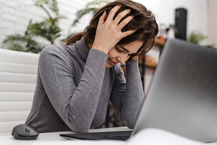 Frustrated employee holding head at desk, realizing new boss expects her to actually work in an office setting. Frustrated employee holding head at desk, realizing new boss expects her to actually work in an office setting.