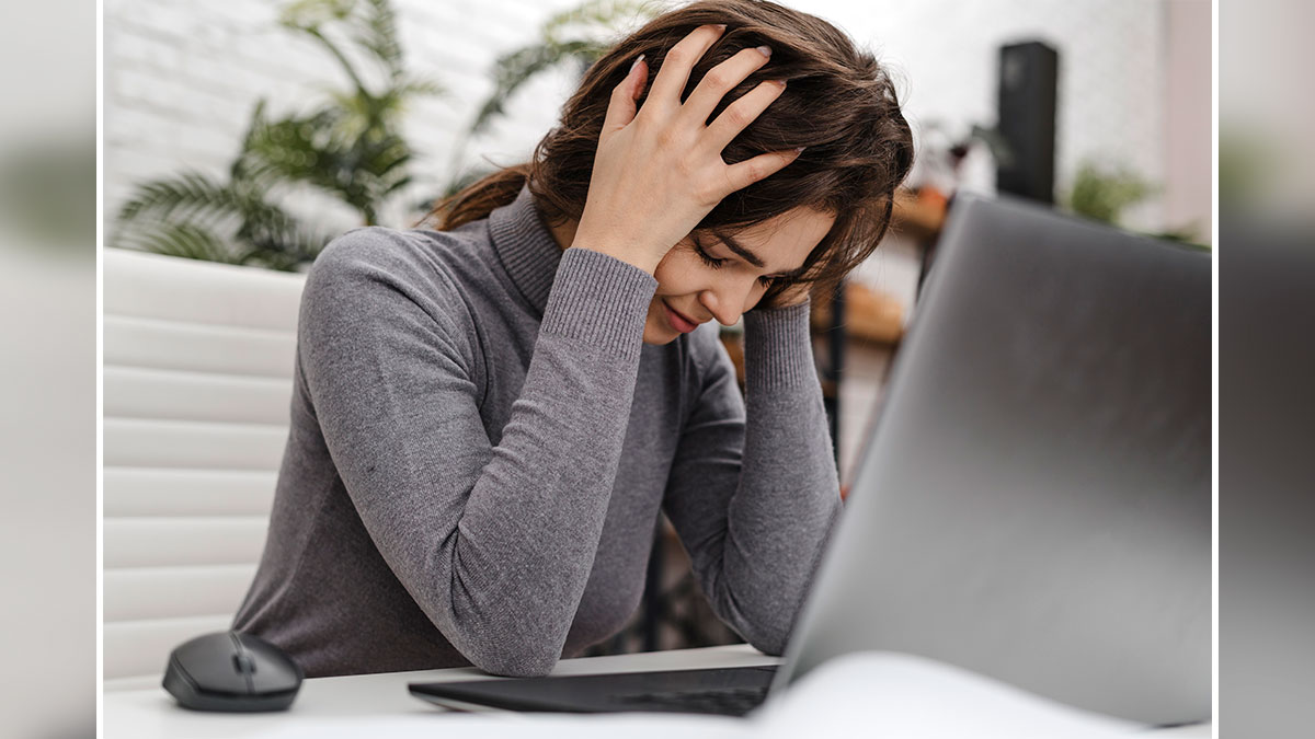 Frustrated employee holding head while sitting at desk with laptop, illustrating lazy employee and new boss expectations.