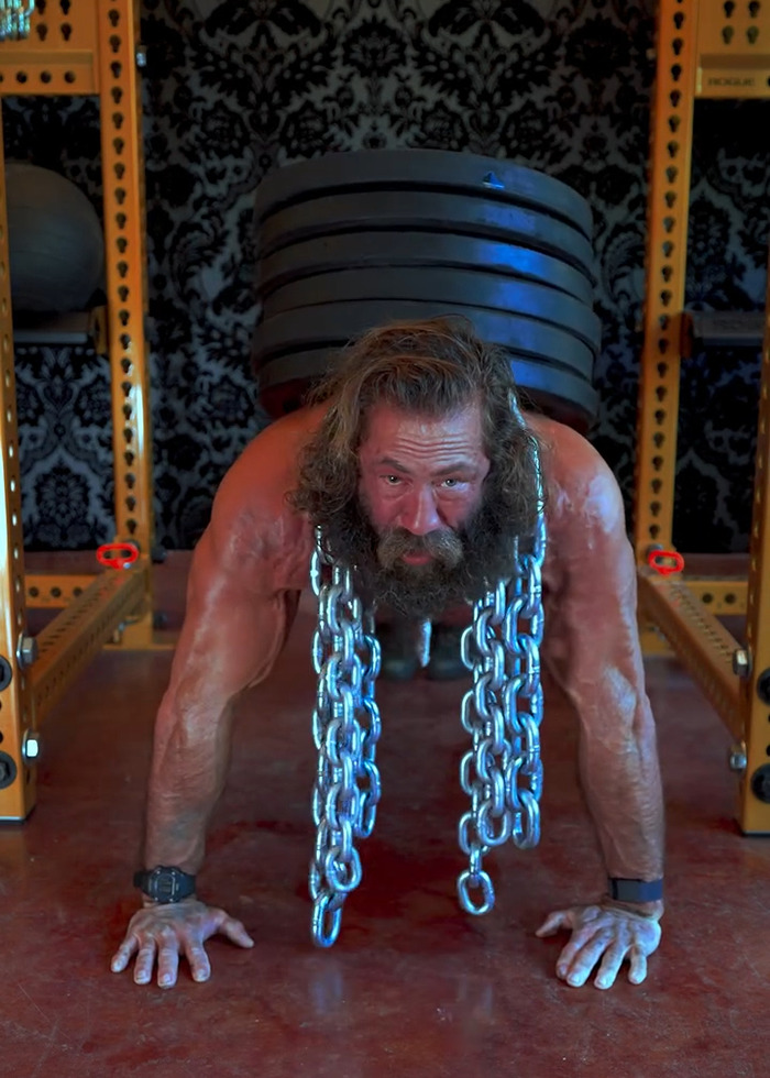 Muscular man with chains around neck and weight plates on back, showcasing strength and raw animal diet lifestyle. Muscular man with chains around neck and weight plates on back, showcasing strength and raw animal diet lifestyle.