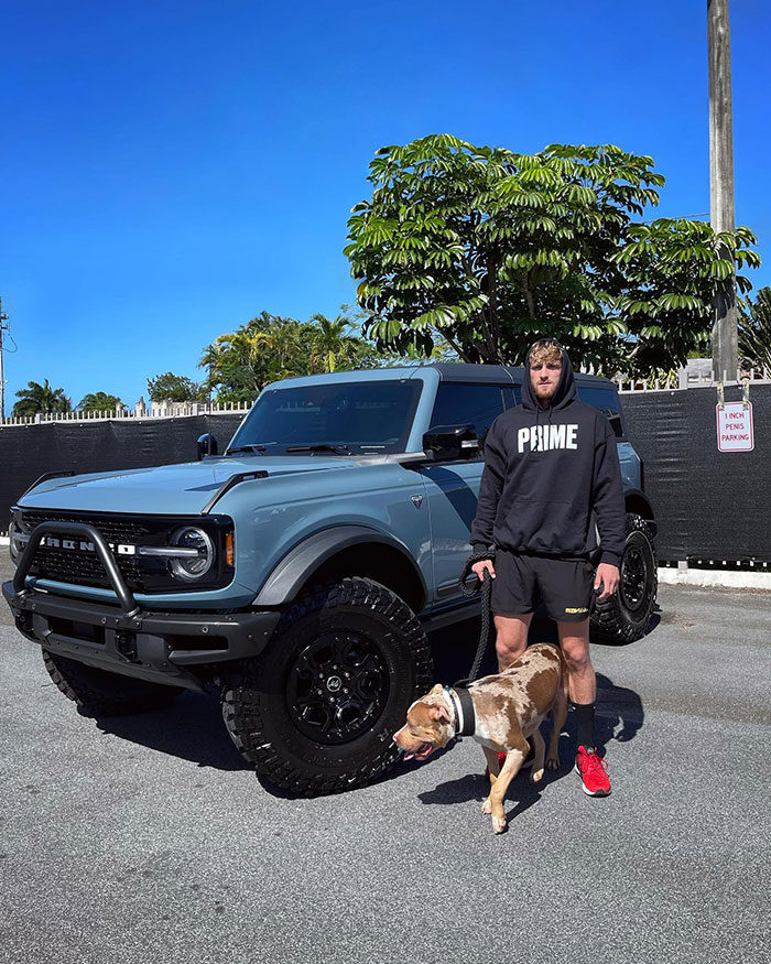 Logan Paul standing with his dog next to a large SUV, showcasing Logan Paul net worth after prime lifestyle.