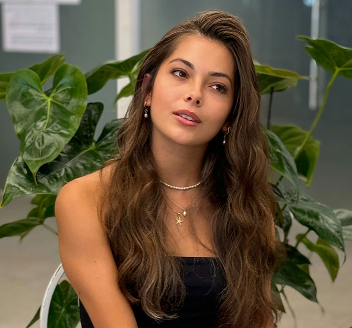 Young woman with long brown hair and pearl jewelry sitting indoors near green plants, reflecting on losing pretty privilege Young woman with long brown hair and pearl jewelry sitting indoors near green plants, reflecting on losing pretty privilege