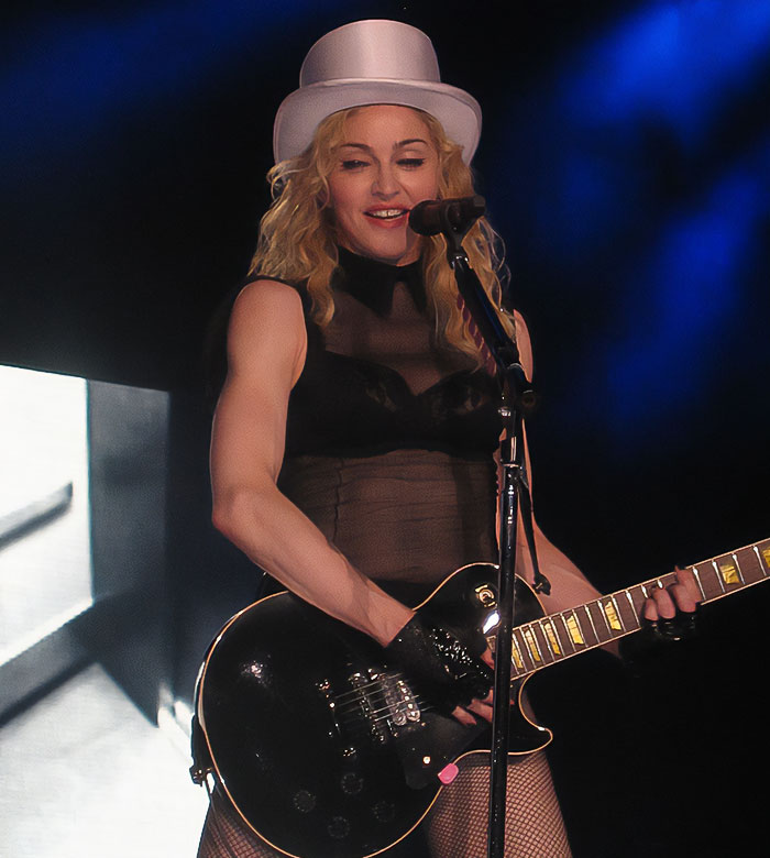 Madonna performing on stage wearing a white hat and playing guitar, fans notice the famous gap missing from her face Madonna performing on stage wearing a white hat and playing guitar, fans notice the famous gap missing from her face