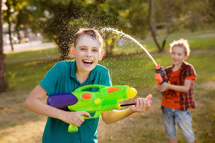 Two kids having fun outdoors playing with colorful water guns in a sunny garden setting.