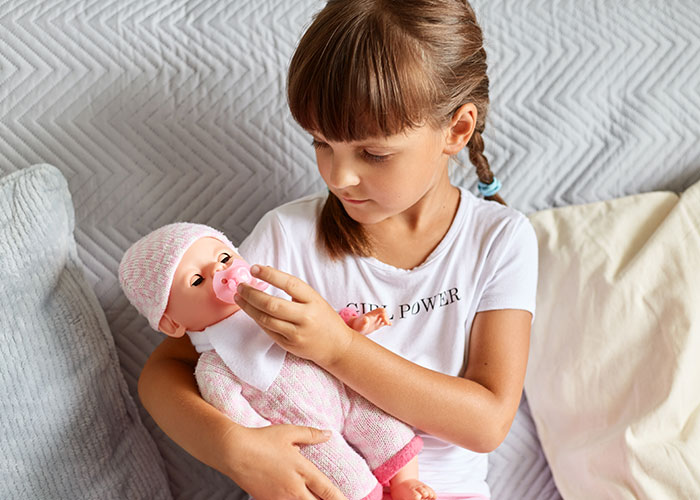 Young girl playing with a baby doll, reflecting pregnancy-obsessed child receiving a weird gift from MIL. Young girl playing with a baby doll, reflecting pregnancy-obsessed child receiving a weird gift from MIL.