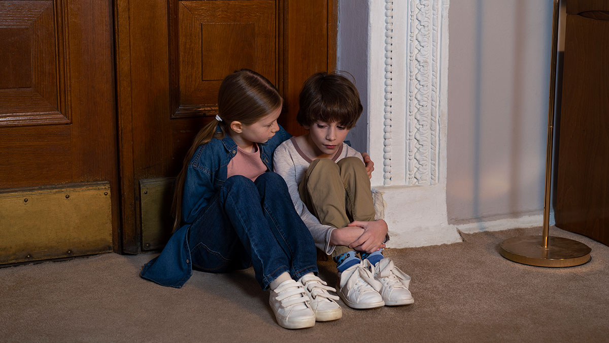 Two worried children sitting on the floor against a door, illustrating concern in a possible family neglect situation.