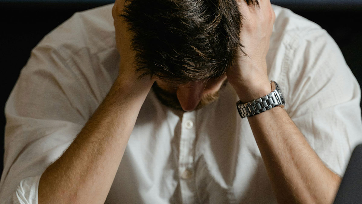 Stressed man holding his head in hands, illustrating consequences of manager told staff not to fill empty shelves dilemma.