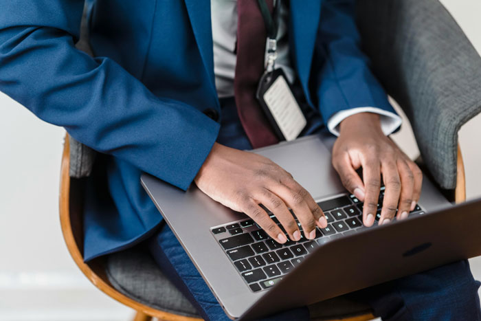Manager typing on laptop, wearing blue suit and an ID badge, representing workplace conflict and baseless claims scenario. Manager typing on laptop, wearing blue suit and an ID badge, representing workplace conflict and baseless claims scenario.