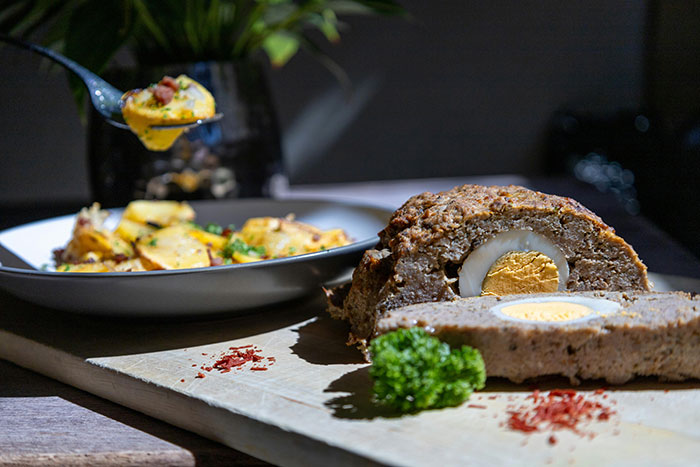 Meat dish with boiled egg center served on wooden board with a side of roasted potatoes, highlighting teen son eating meat. Meat dish with boiled egg center served on wooden board with a side of roasted potatoes, highlighting teen son eating meat.