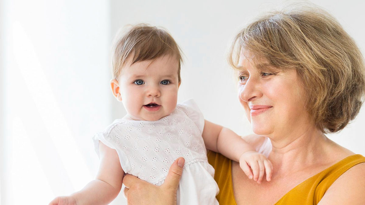 Older woman holding baby indoors, capturing moment related to mom suspecting MIL pretending to be babyu2019s mom.